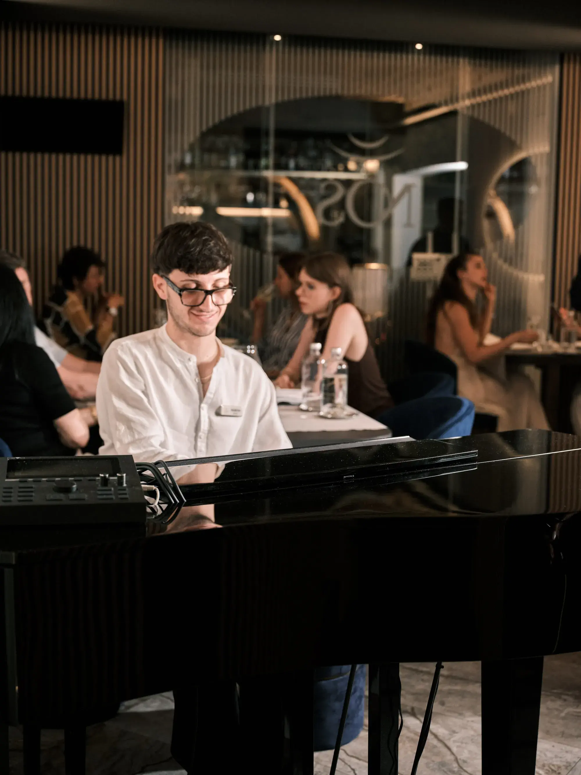 Martin ao piano de cauda no NOS, a sala a jantar atrás dele e o letreiro NOS ao fundo