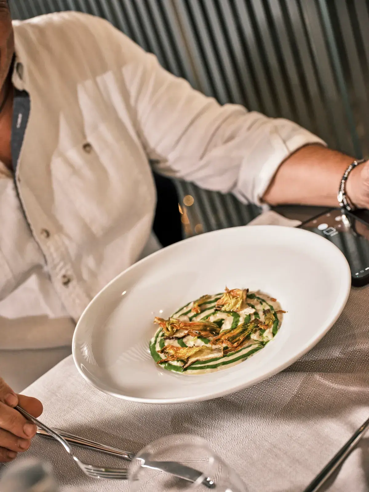 Ospite a tavola davanti a un piatto di verdure con crema alle erbe e croccante, su grande piatto bianco
